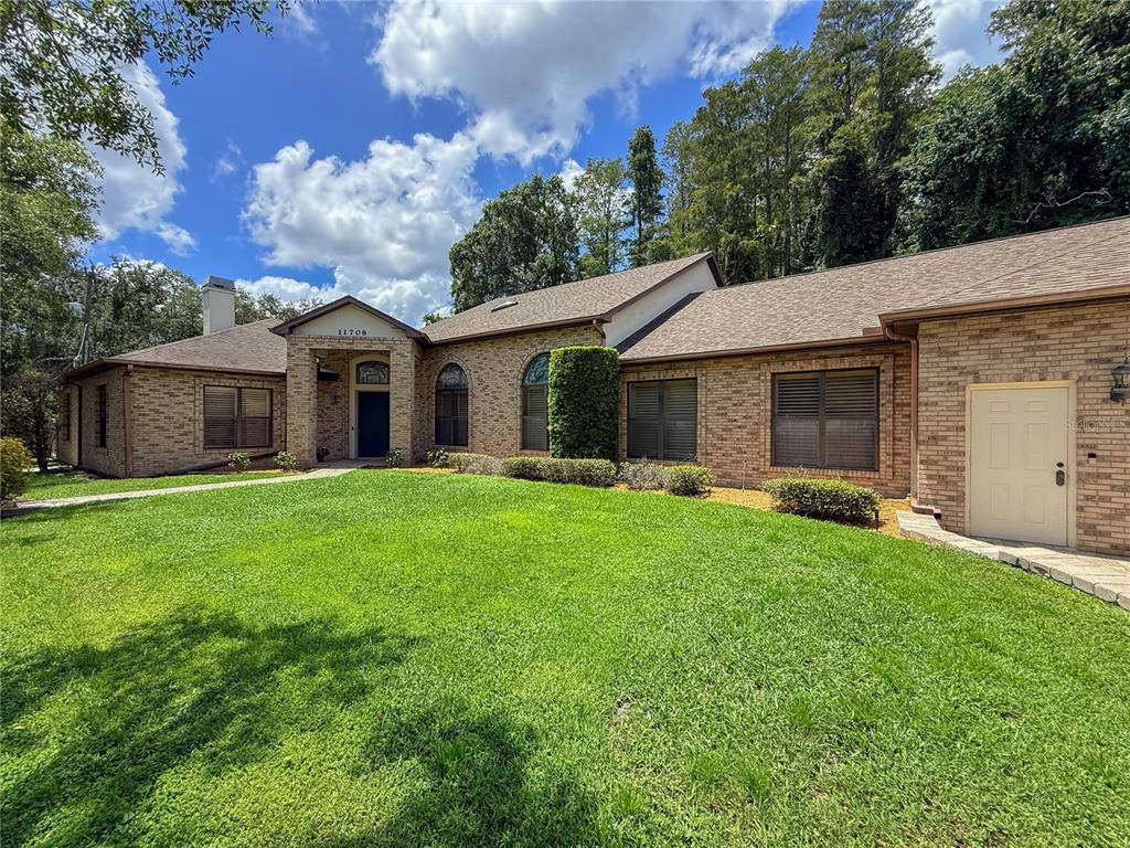 A single-story brick house with a large front lawn and a prominent arched entryway — 11708 ORANGE GROVE DRIVE, TAMPA, FL