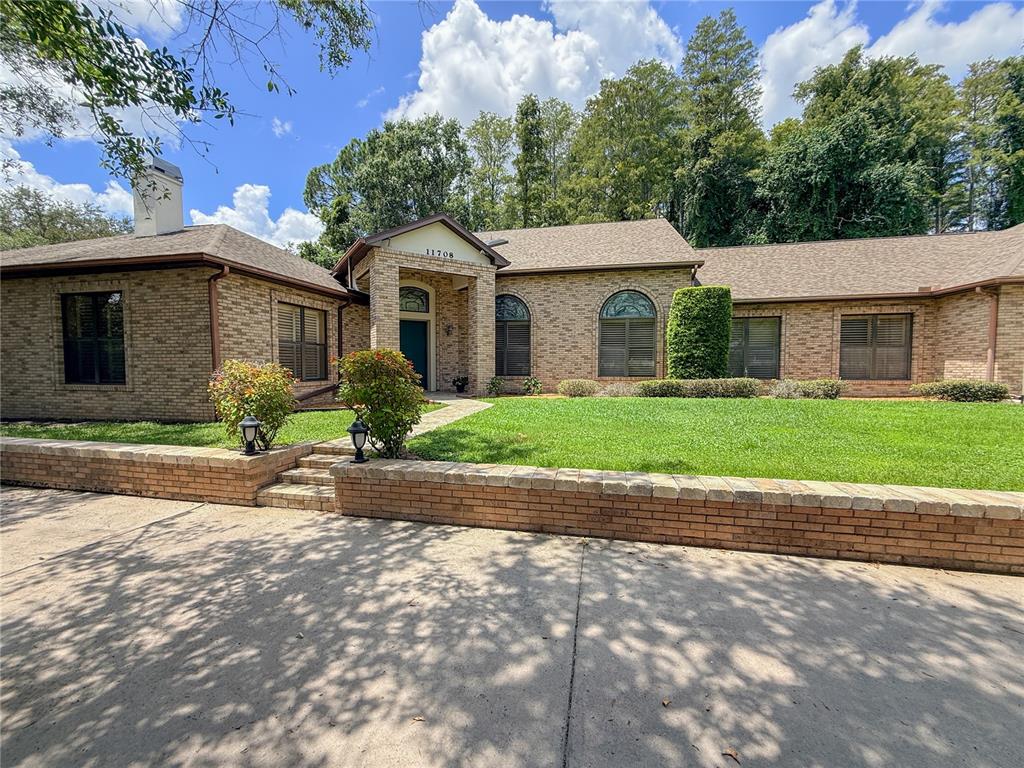 A single-story brick house features a covered entryway, arched windows, and a low retaining wall — 11708 ORANGE GROVE DRIVE, TAMPA, FL