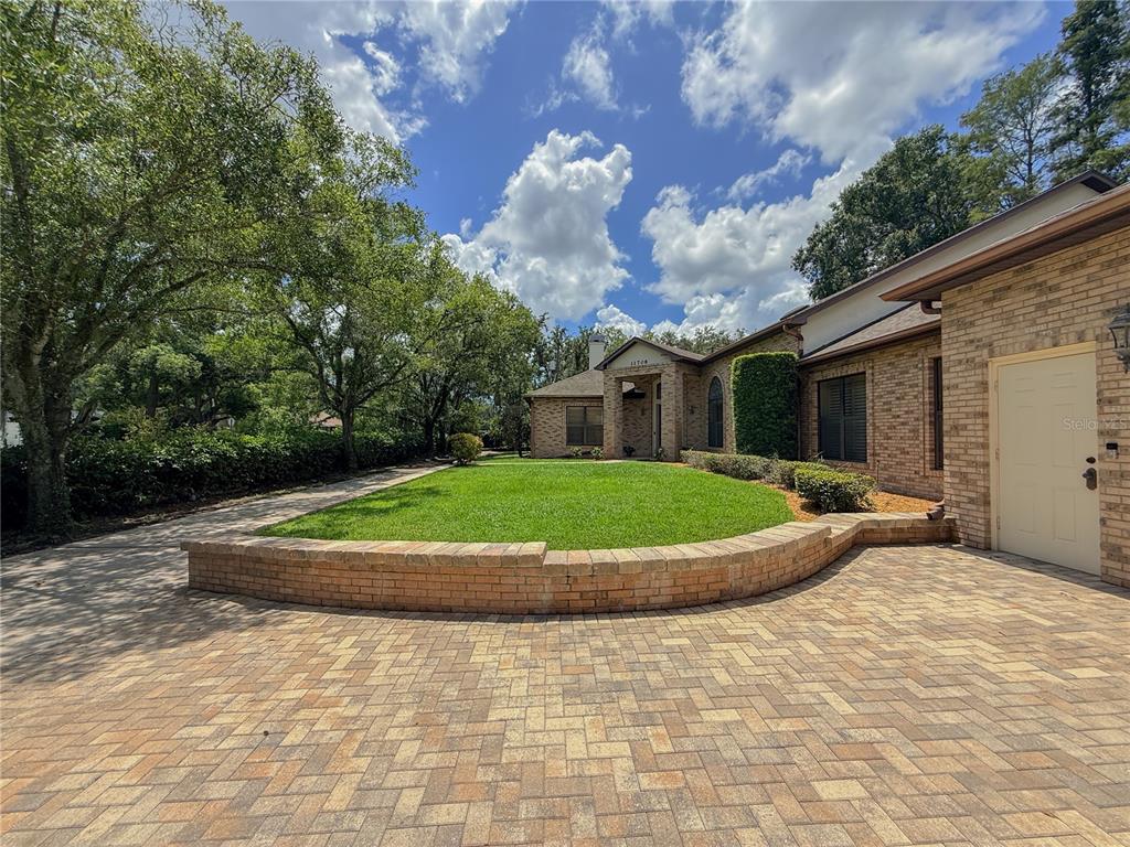 A brick house with a paver driveway and a curved retaining wall bordering a lawn — 11708 ORANGE GROVE DRIVE, TAMPA, FL