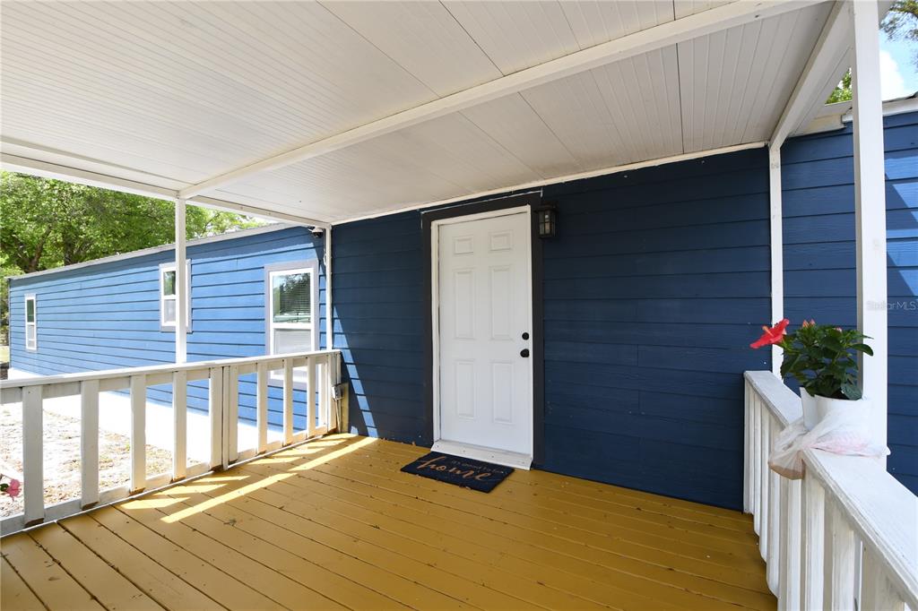 A covered wooden porch with white railings leads to a white door on a blue house — 7457 NE HIGHWAY 349, OLD TOWN, FL