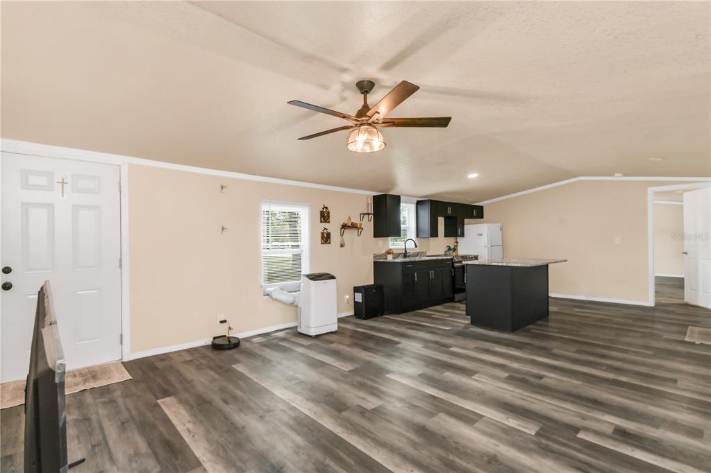 An open-concept living area features wood-look flooring, a ceiling fan, and a kitchen with dark cabinets — 7457 NE HIGHWAY 349, OLD TOWN, FL