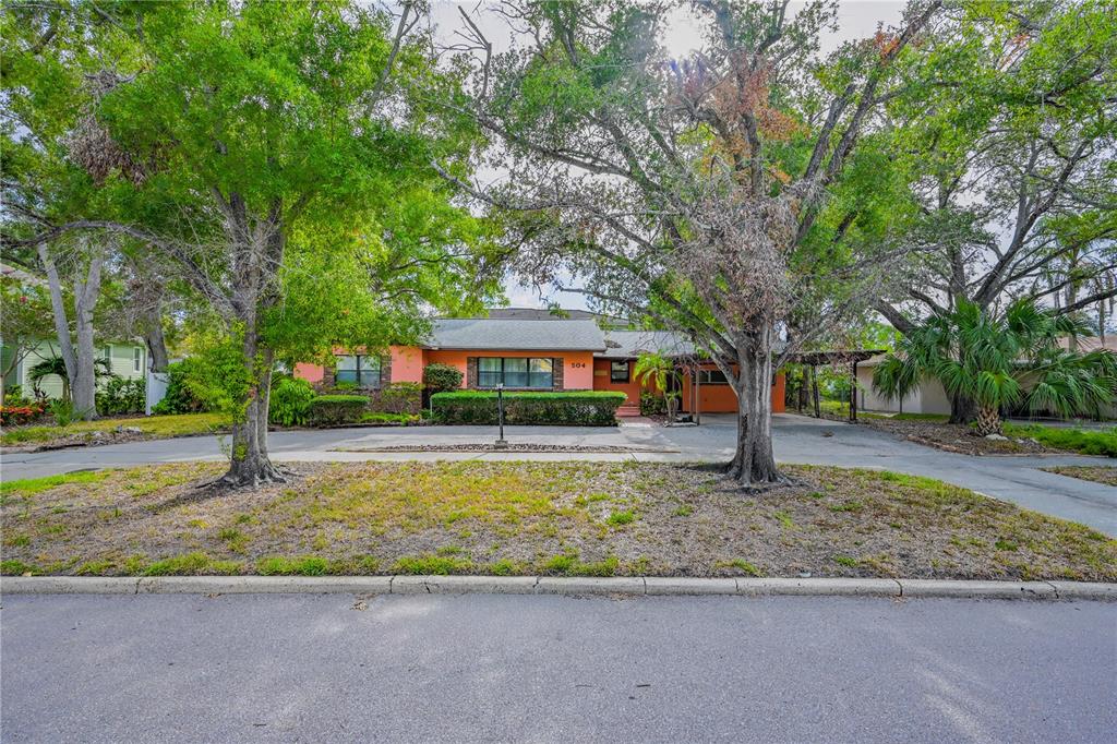 A single-story orange house with a carport sits behind two large trees and a driveway — 504 W DAVIS BOULEVARD, TAMPA, FL