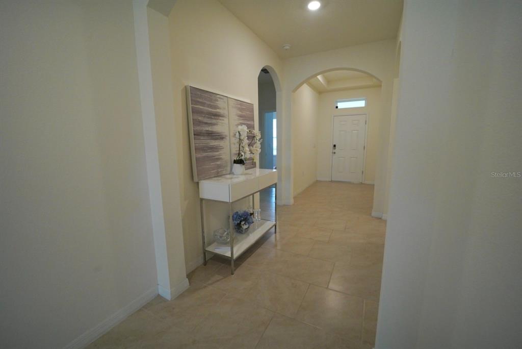 A tiled entryway features an arched hallway, a console table with artwork, and a front door — 6946 AUDOBON OSPREY COVE, HARMONY, FL