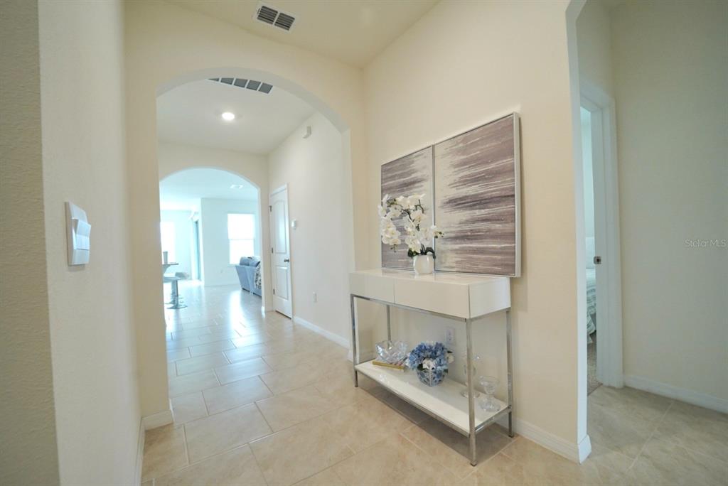 A tiled entryway features an arched hallway, a white console table, and abstract wall art — 6946 AUDOBON OSPREY COVE, HARMONY, FL