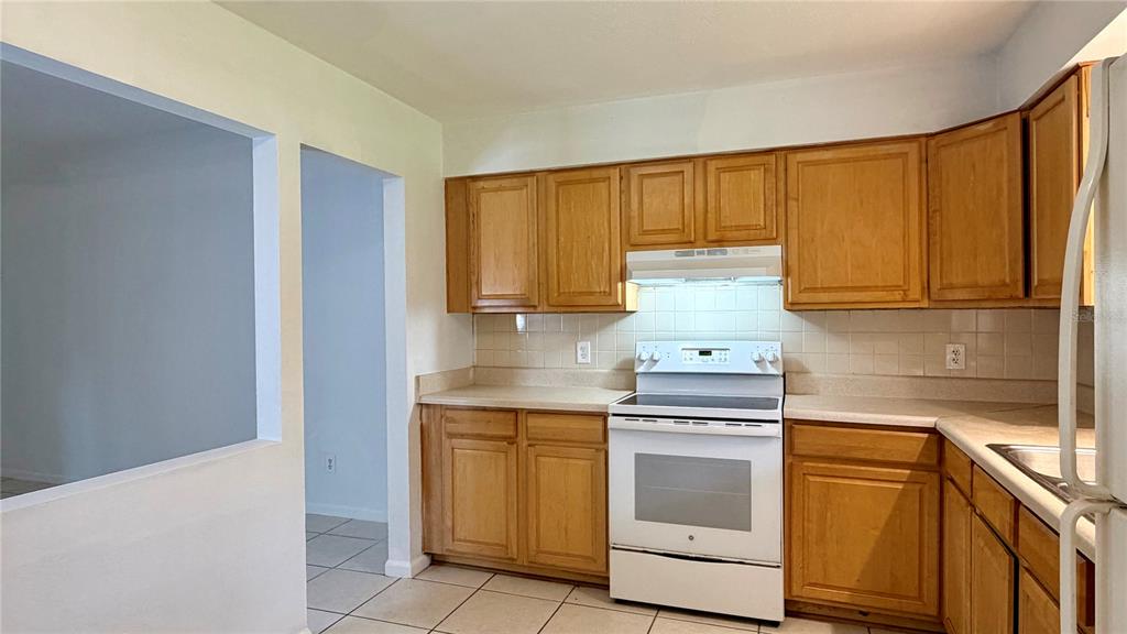 A kitchen features light wood cabinets, white appliances, and a tiled backsplash — 601 SOLDIER SQUARE, CASSELBERRY, FL