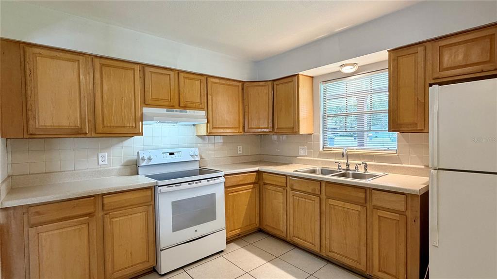 A kitchen features light wood cabinets, white appliances, a double sink, and tiled countertops — 601 SOLDIER SQUARE, CASSELBERRY, FL