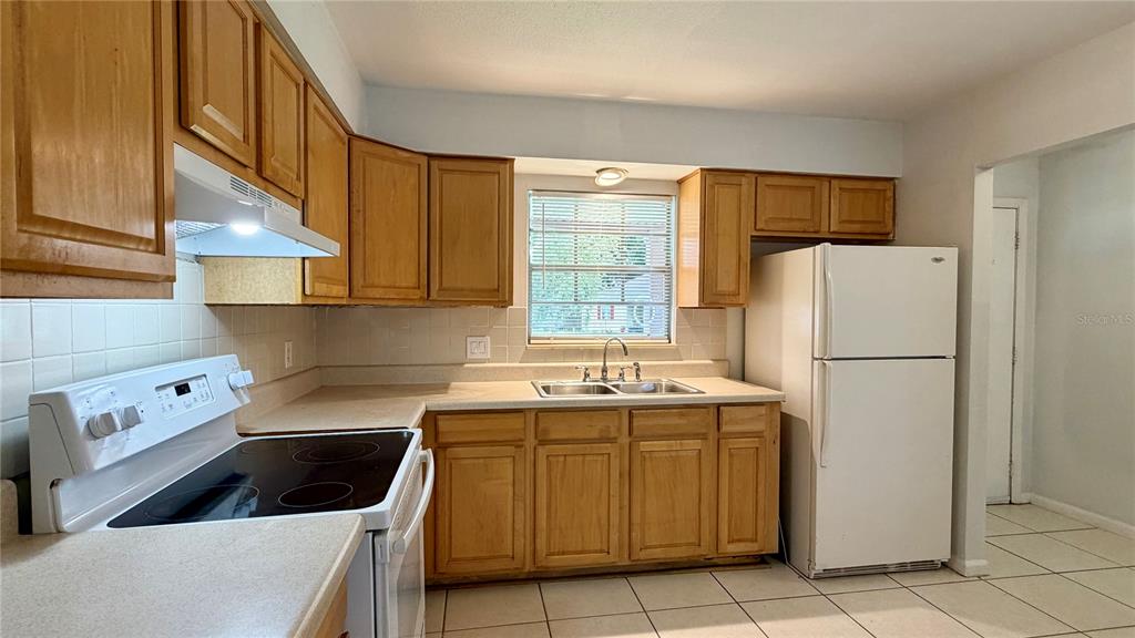 A kitchen features light wood cabinets, white appliances, a double sink, and tiled flooring — 601 SOLDIER SQUARE, CASSELBERRY, FL