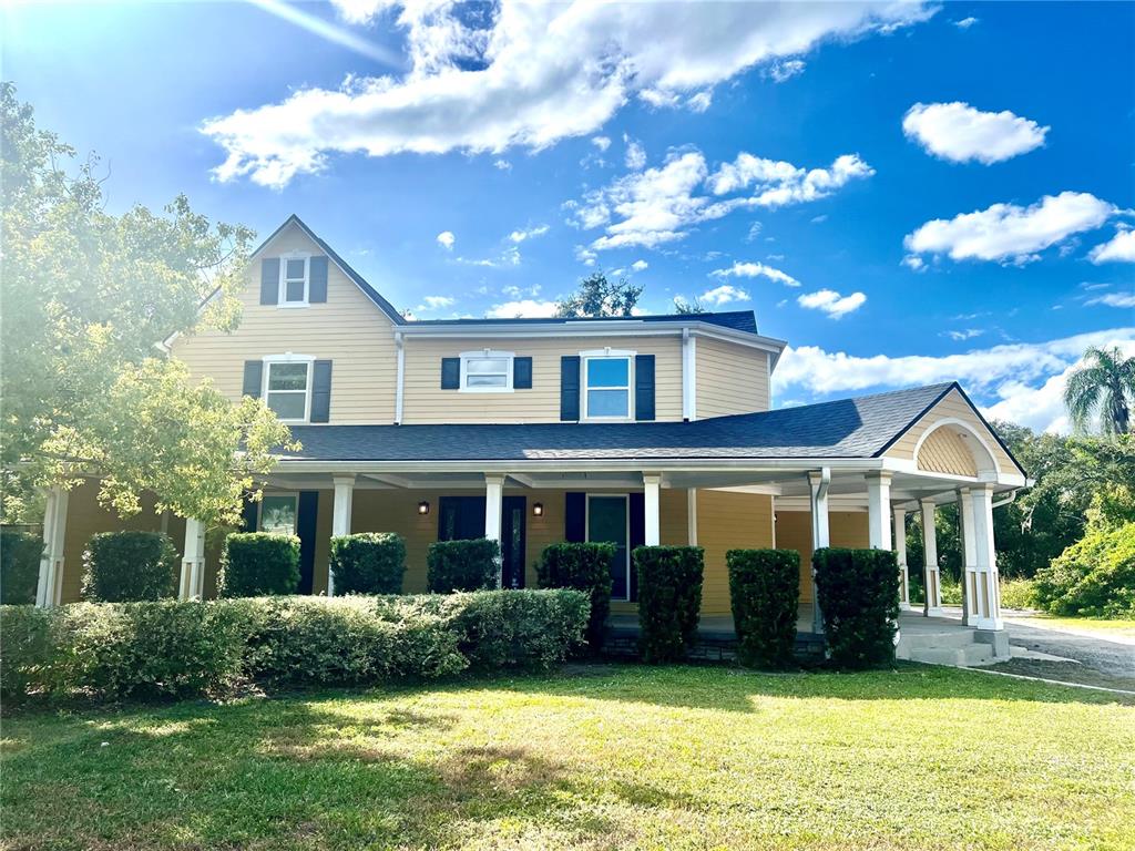 A two-story yellow house with a large front porch and a side carport — 1109 BELCHER ROAD, PALM HARBOR, FL