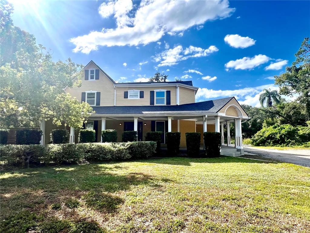A two-story yellow house with a large front porch and a carport under a blue sky — 1109 BELCHER ROAD, PALM HARBOR, FL