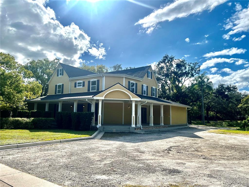 A two-story yellow house with a wraparound porch and a gravel driveway — 1109 BELCHER ROAD, PALM HARBOR, FL