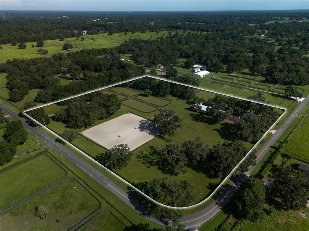 An aerial view shows a fenced property with a riding arena, house, and mature trees — 3680 NW 115TH AVENUE, OCALA, FL