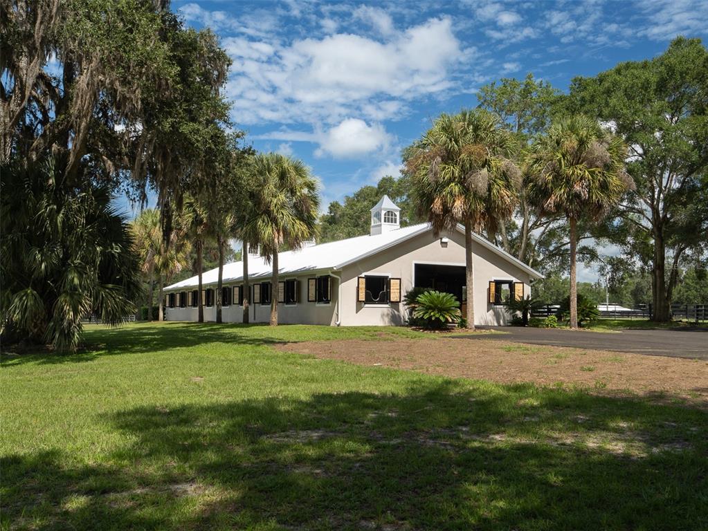 A white horse barn with a metal roof stands on a grassy lot with palm trees — 3680 NW 115TH AVENUE, OCALA, FL