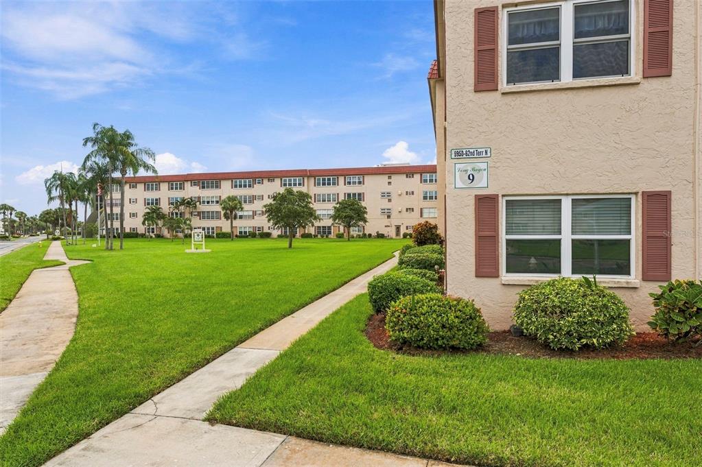 A view of a multi-story apartment building exterior with a lawn and sidewalk — 9950 62ND TERRACE N UNIT 408, ST PETERSBURG, FL
