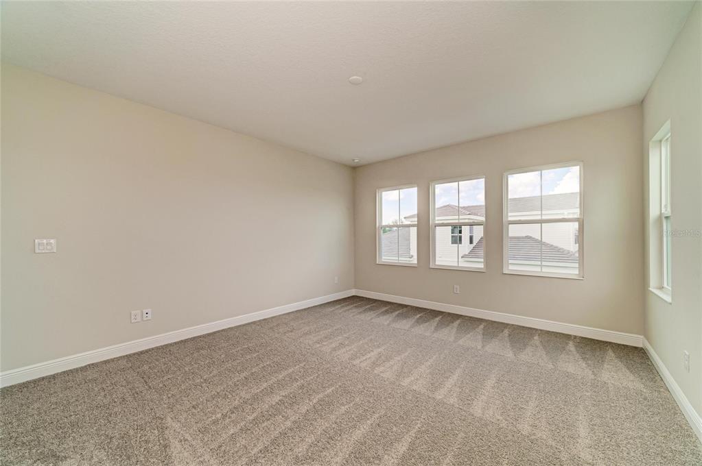 An empty room with beige walls, gray carpet, and multiple windows overlooking neighboring houses — 10245 CROSS RIVER TRAIL, PARRISH, FL