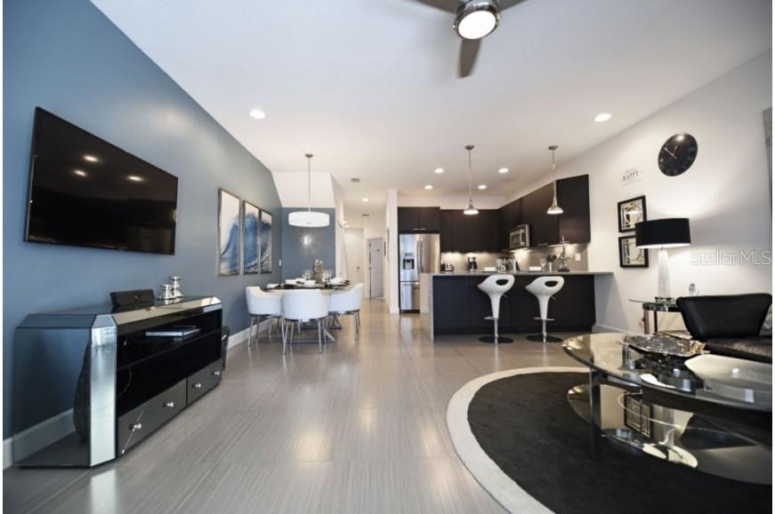 An open-concept living and dining area features a modern kitchen with dark cabinetry and island — 17440 PLACIDITY AVENUE, CLERMONT, FL
