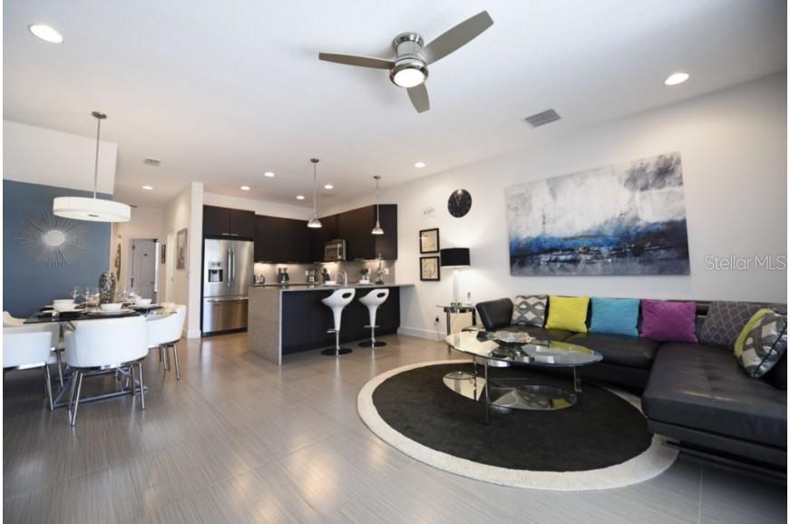 An open-concept living and dining area features dark cabinetry, stainless appliances, and modern decor — 17440 PLACIDITY AVENUE, CLERMONT, FL