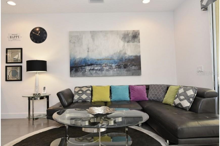 A living room features a dark leather sectional, a glass coffee table, and abstract wall art — 17440 PLACIDITY AVENUE, CLERMONT, FL