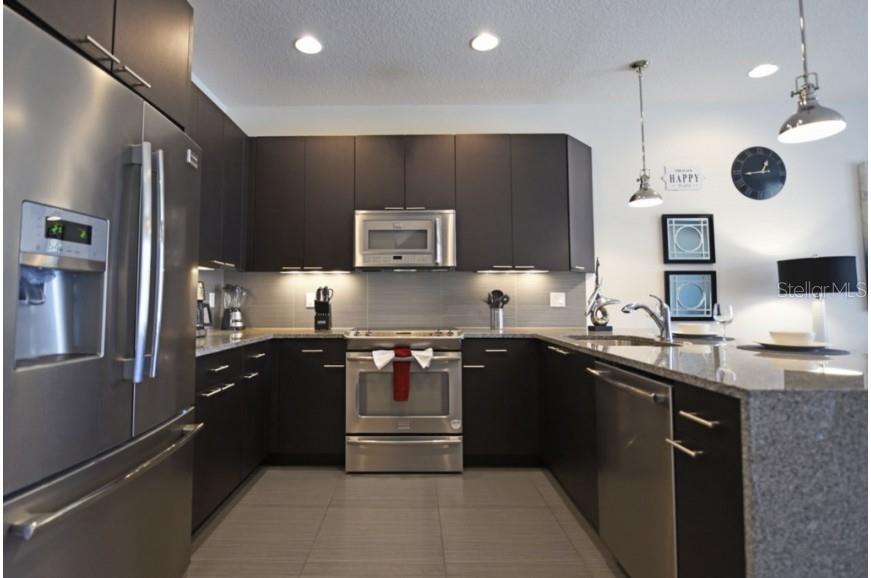 A modern kitchen features dark cabinetry, stainless steel appliances, granite countertops, and tile flooring — 17440 PLACIDITY AVENUE, CLERMONT, FL