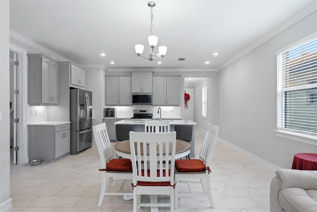 A kitchen features gray cabinets, a central island, and a dining table with white chairs — 113 MOSCATA WAY, NOKOMIS, FL