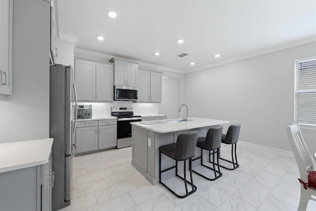 A modern kitchen features gray cabinets, white countertops, a central island, and light tile flooring — 113 MOSCATA WAY, NOKOMIS, FL