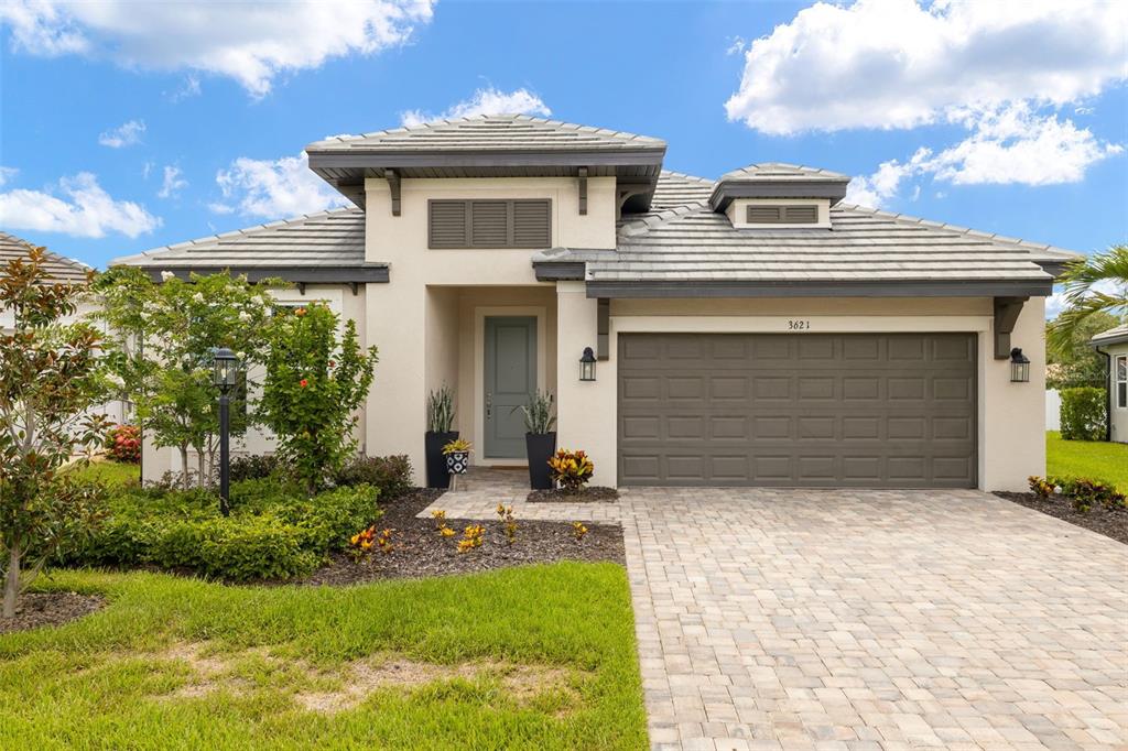 A single-story house with a beige stucco exterior, gray tile roof, and a two-car garage — 3621 WILD BLOSSOM PLACE, PARRISH, FL