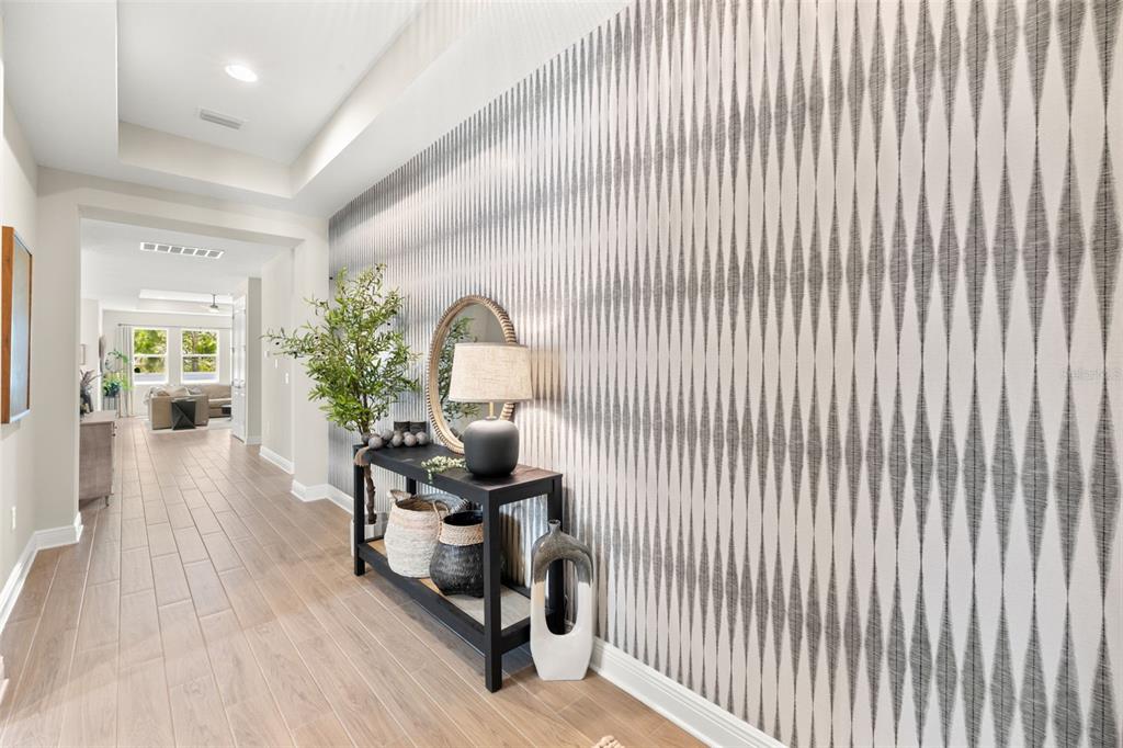 A hallway features wood-look tile flooring and a wall covered in patterned gray wallpaper — 3621 WILD BLOSSOM PLACE, PARRISH, FL