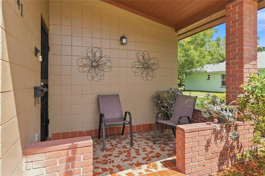 A covered porch features a mosaic tile floor, brick accents, and two outdoor chairs — 841 WOODEN BOULEVARD, ORLANDO, FL