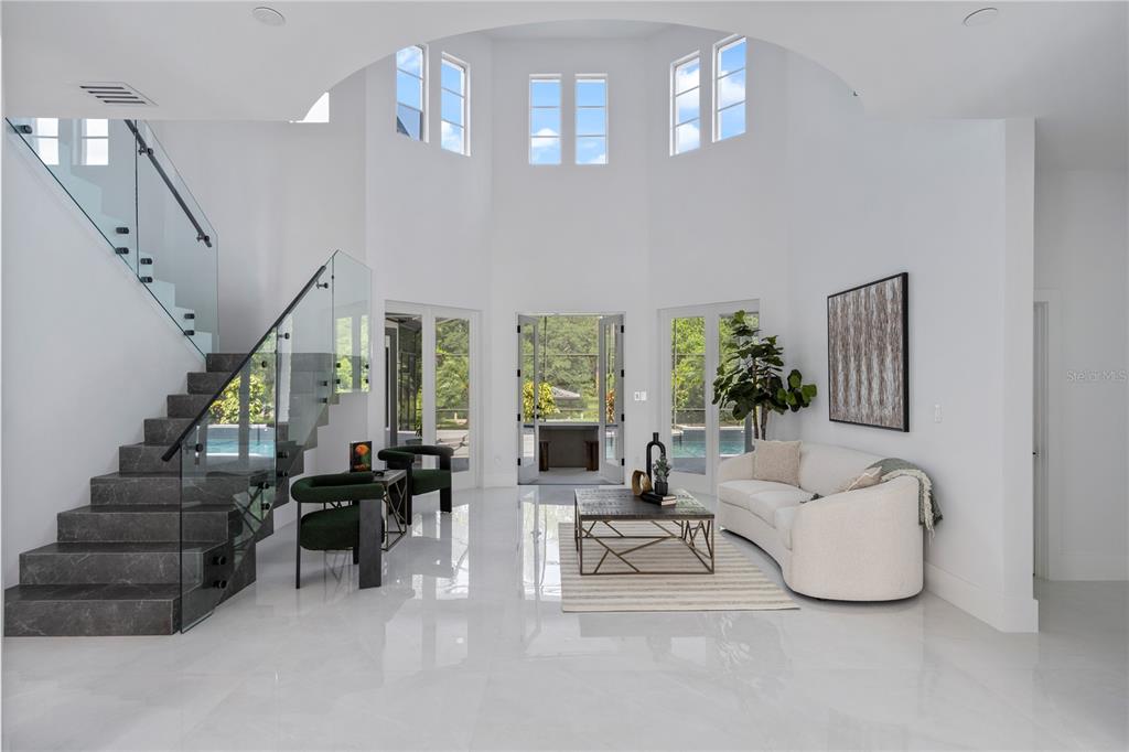 A bright, modern living room features a floating staircase, high vaulted ceilings, and glass doors — 10849 EMERALD CHASE DRIVE, ORLANDO, FL