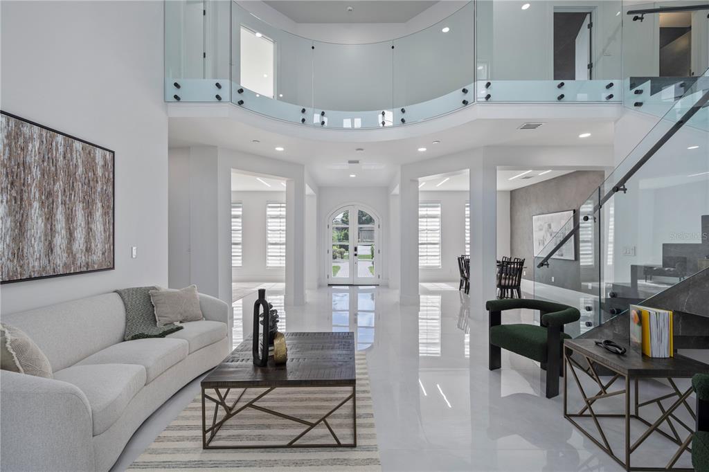 A bright, modern foyer features white tile floors, a glass-railed balcony, and a seating area — 10849 EMERALD CHASE DRIVE, ORLANDO, FL