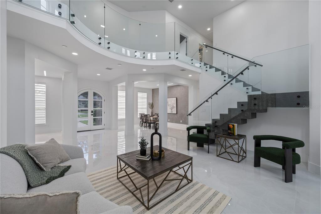 A modern living room features a floating staircase, glass railings, and white tile flooring — 10849 EMERALD CHASE DRIVE, ORLANDO, FL