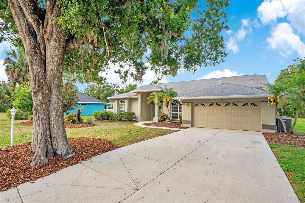 A single-story house with a beige stucco exterior, a two-car garage, and a large tree — 3404 RIVER WOODS DRIVE, PARRISH, FL