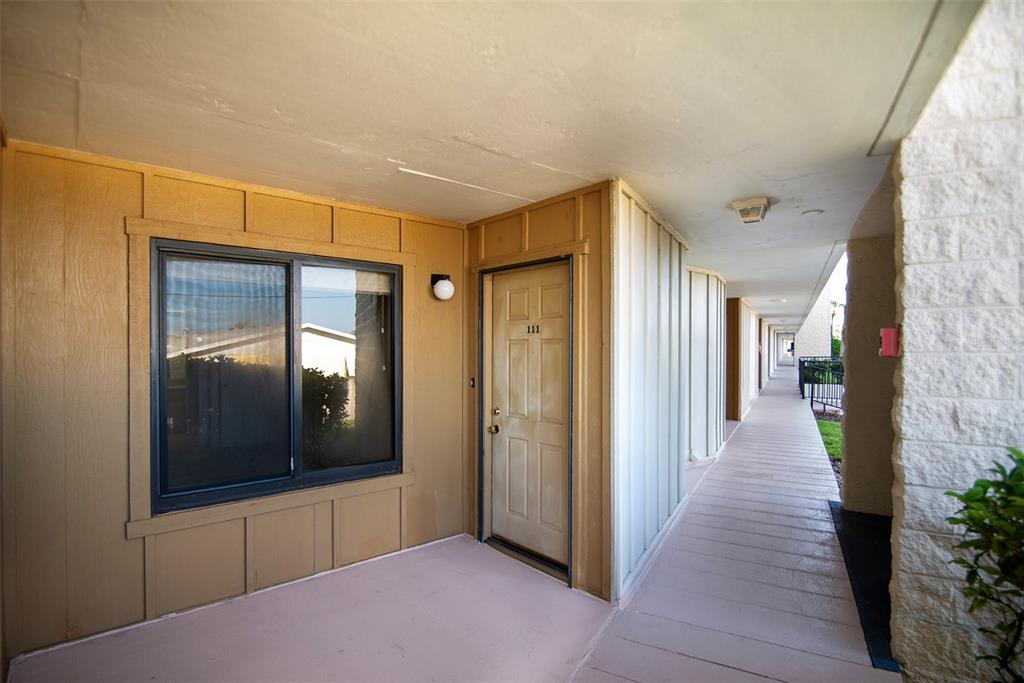 An exterior view of an apartment entrance with a tan door numbered 111 — 2600 OCEAN SHORE BOULEVARD UNIT 111, ORMOND BEACH, FL