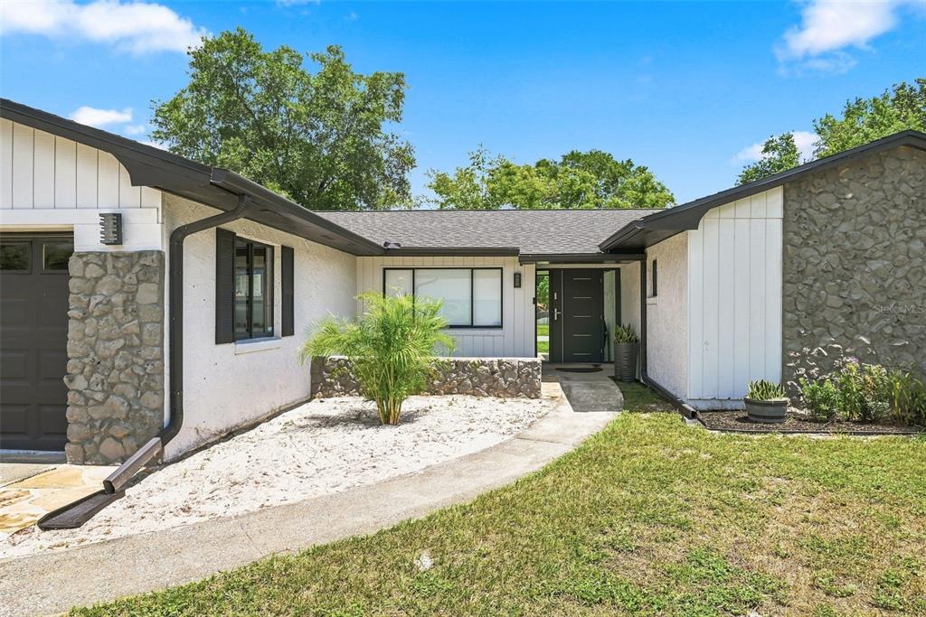 A single-story house exterior features white siding, stone accents, a dark front door, and landscaping — 6349 MARLBERRY DRIVE, ORLANDO, FL