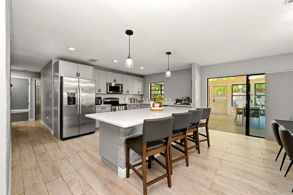 A modern kitchen features a large white island, stainless steel appliances, and light wood-look flooring — 6349 MARLBERRY DRIVE, ORLANDO, FL