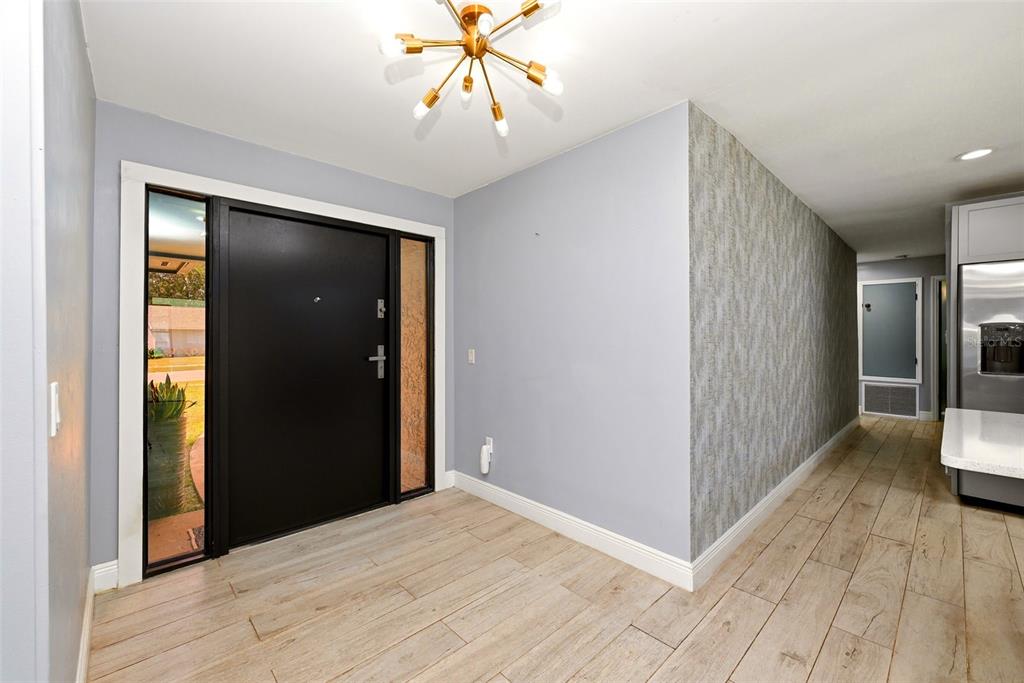 An entryway with light wood-look tile flooring, a black front door, and a textured accent wall — 6349 MARLBERRY DRIVE, ORLANDO, FL