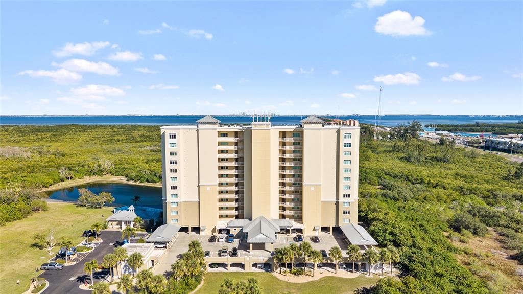 An aerial view shows a tall, tan residential building surrounded by greenery and a pond — 10851 MANGROVE CAY LANE NE UNIT 1112, ST PETERSBURG, FL