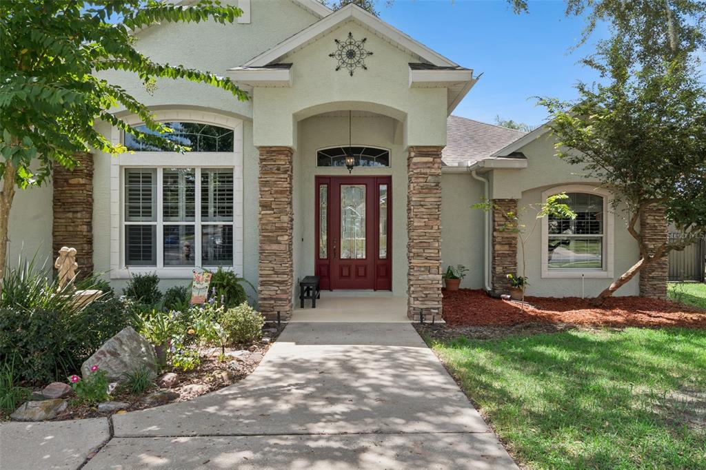 A light-colored house exterior features a red front door, stone columns, and a concrete walkway — 106 OAK HAVEN CIRCLE, DELAND, FL