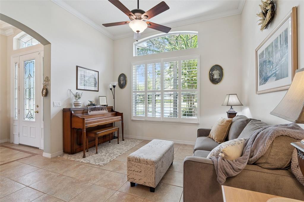 A living room features a piano, a gray sofa, tile flooring, and plantation shutters — 106 OAK HAVEN CIRCLE, DELAND, FL