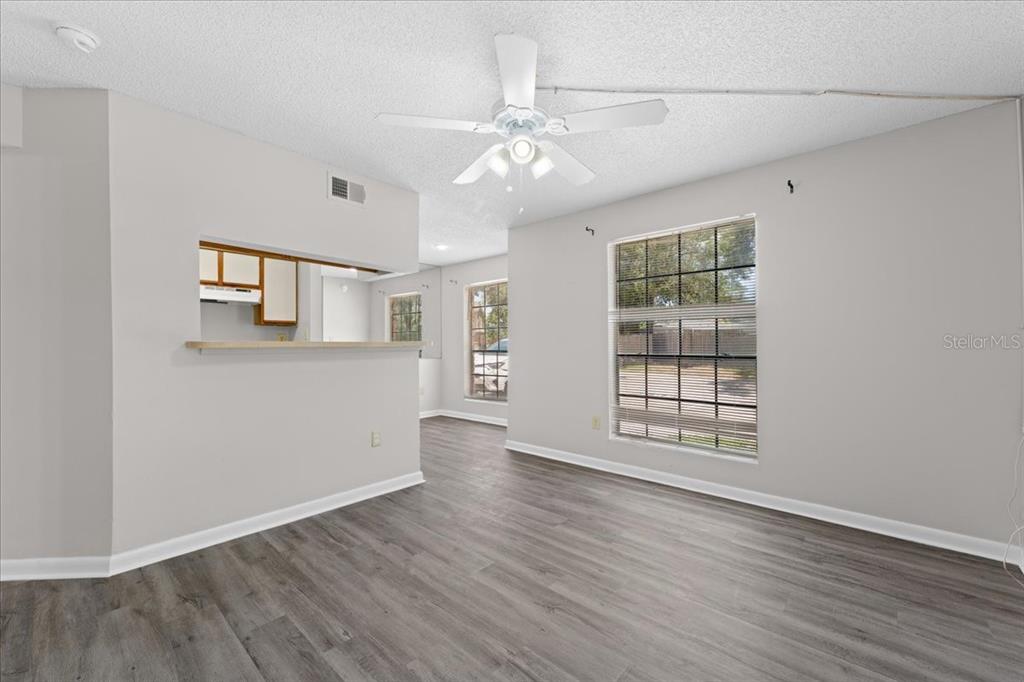 An empty living room features gray wood-look flooring, light walls, and a ceiling fan — 8641 FANCY FINCH DRIVE UNIT 102, TAMPA, FL