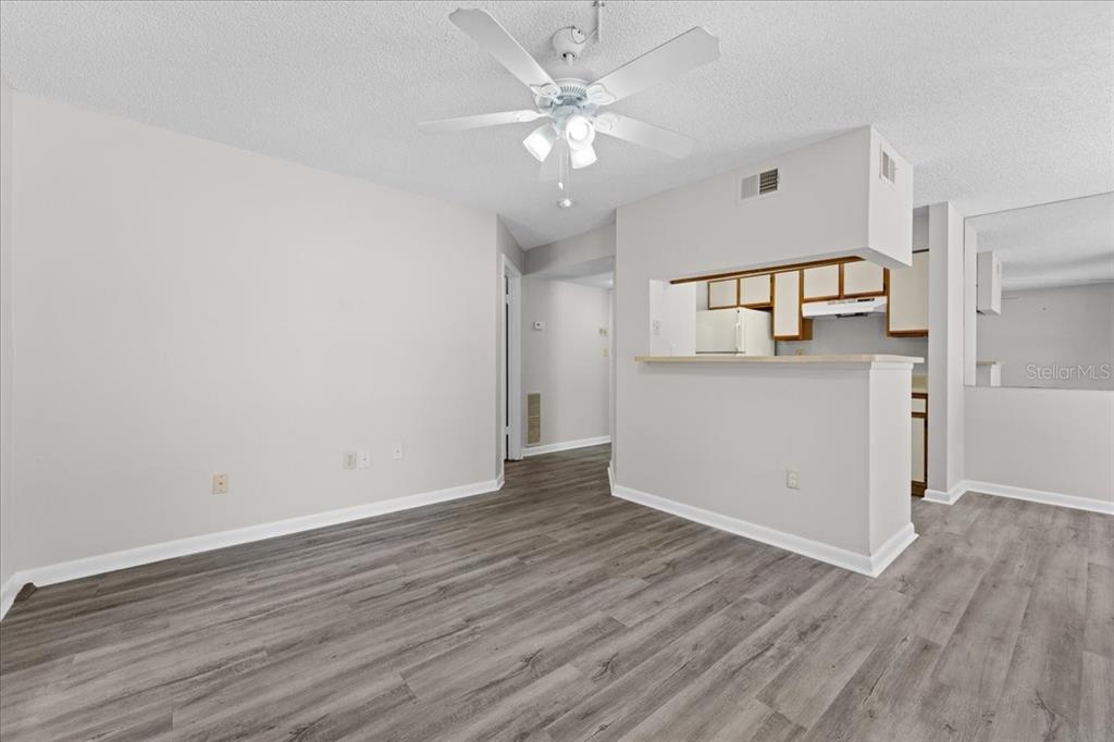 An empty living room features gray wood-look flooring, a ceiling fan, and a kitchen pass-through — 8641 FANCY FINCH DRIVE UNIT 102, TAMPA, FL