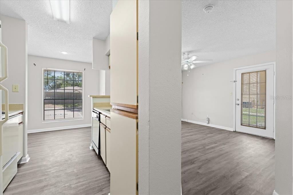 A kitchen with light cabinets and wood-look flooring opens into a living area with a door — 8641 FANCY FINCH DRIVE UNIT 102, TAMPA, FL