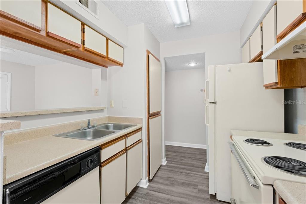 A galley-style kitchen features white cabinets, laminate countertops, a double sink, and white appliances — 8641 FANCY FINCH DRIVE UNIT 102, TAMPA, FL