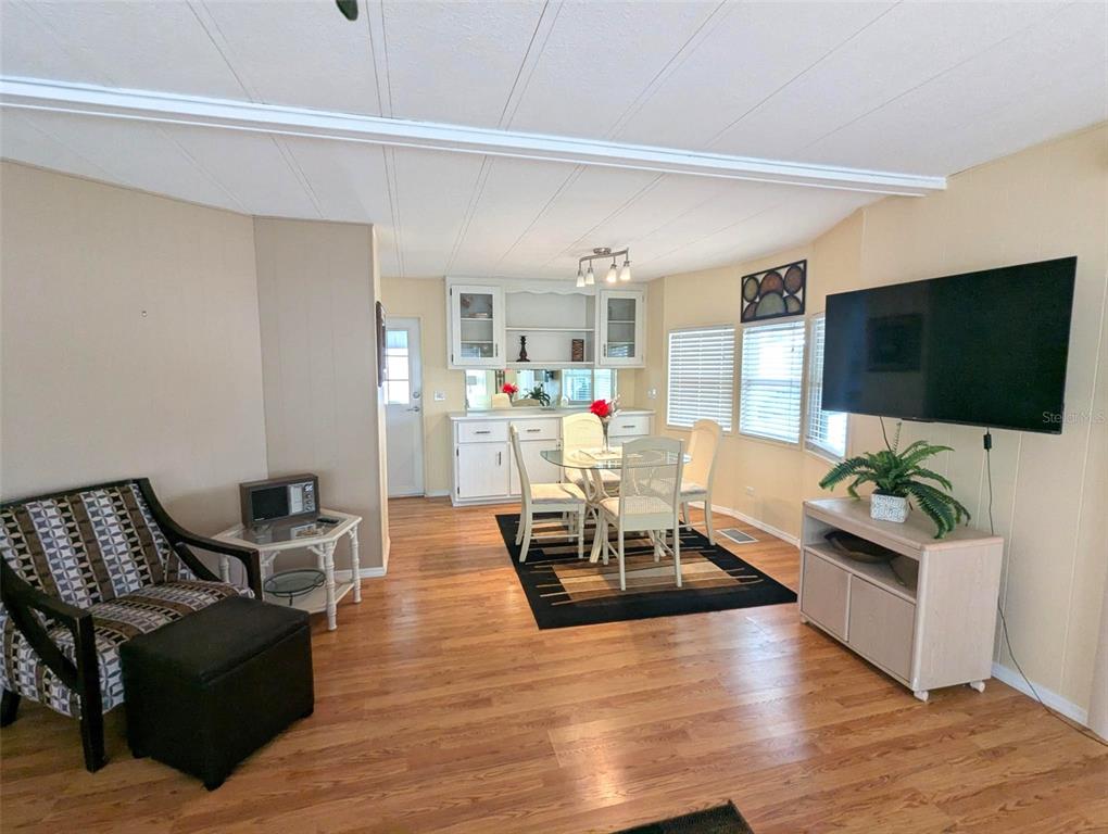 A living and dining area with wood-look flooring, a wall-mounted television, and white cabinetry — 2100 KINGS HIGHWAY UNIT 137, PORT CHARLOTTE, FL