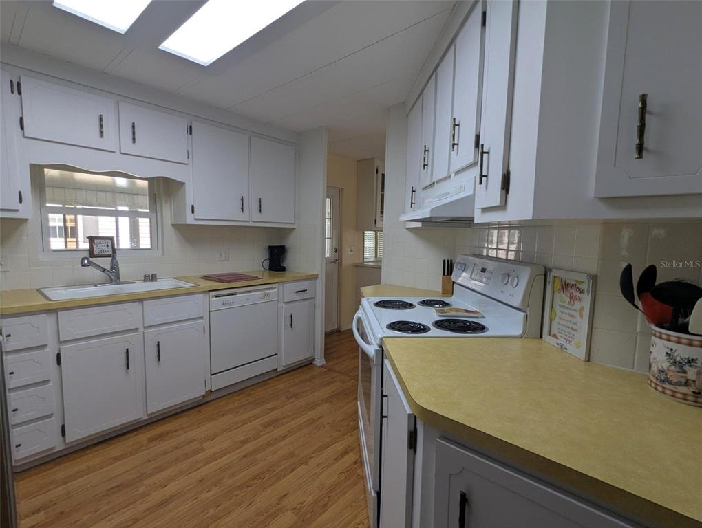 A kitchen features white cabinets, yellow laminate countertops, wood-look flooring, and white appliances — 2100 KINGS HIGHWAY UNIT 137, PORT CHARLOTTE, FL