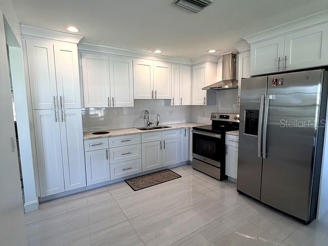 A modern kitchen features white cabinetry, stainless steel appliances, and a dining area with tile floors — 1629 WILLOW RUN, SEBRING, FL