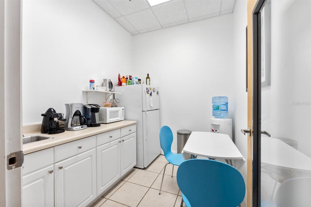 A small office breakroom features white cabinets, a refrigerator, a microwave, and two blue chairs — 8810 COMMODITY CIR UNIT 36, ORLANDO, FL