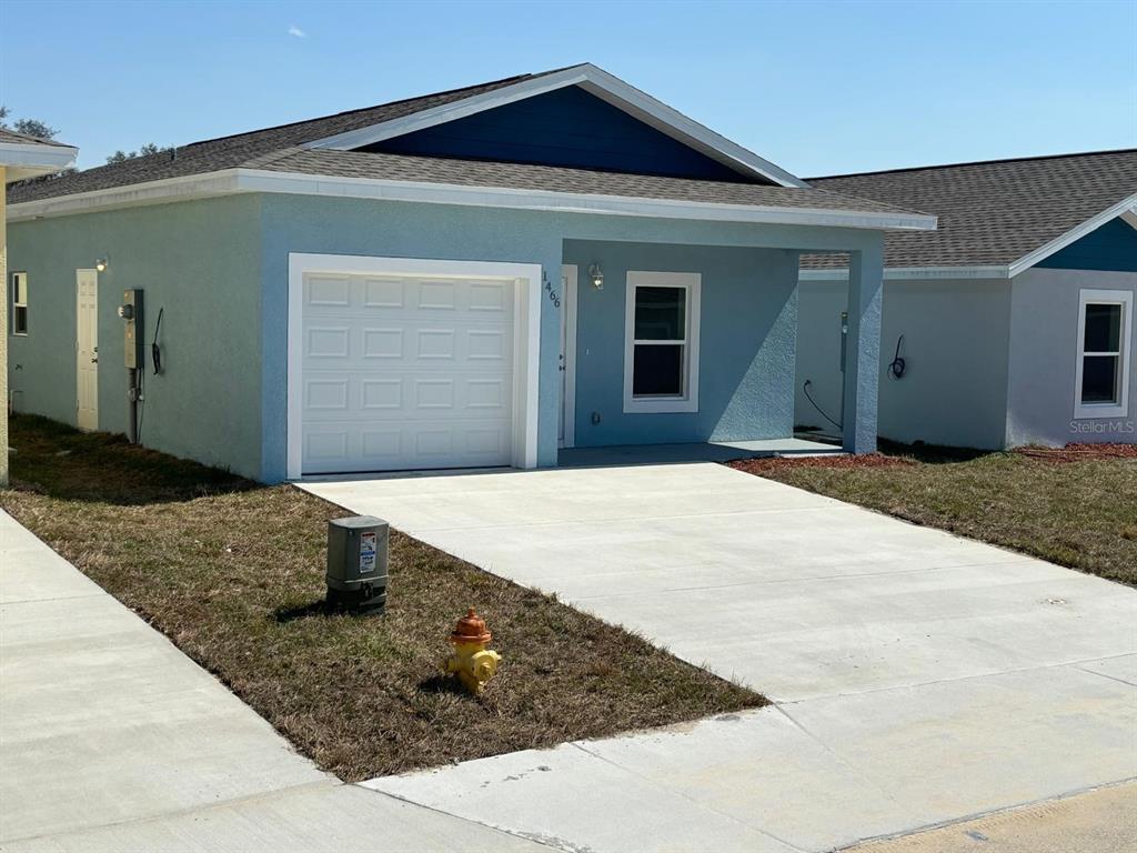 A light blue single-story house features a white garage door and a concrete driveway — 1466 LAS VILLAS BOULEVARD, SEBRING, FL