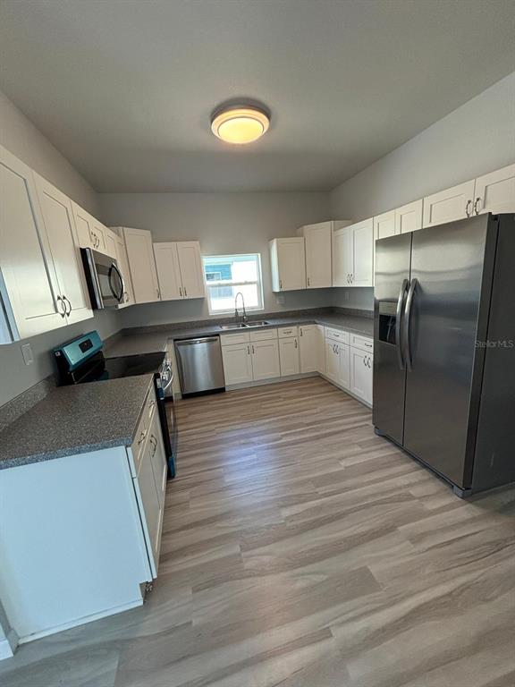 A kitchen features white cabinets, stainless steel appliances, grey countertops, and light wood-look flooring — 1466 LAS VILLAS BOULEVARD, SEBRING, FL