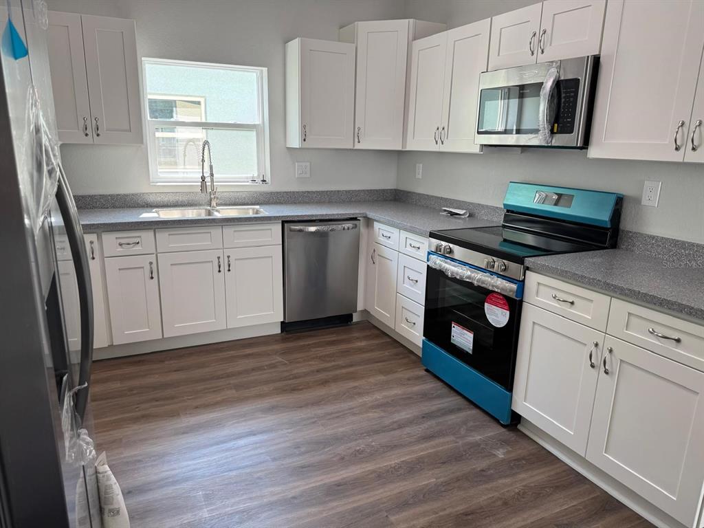 A kitchen with white cabinets, stainless steel appliances, and gray countertops over wood-look flooring — 1466 LAS VILLAS BOULEVARD, SEBRING, FL