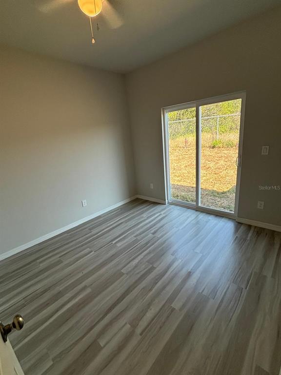 An empty room features light-colored wood-look flooring, neutral walls, a ceiling fan, and sliding glass doors — 1466 LAS VILLAS BOULEVARD, SEBRING, FL